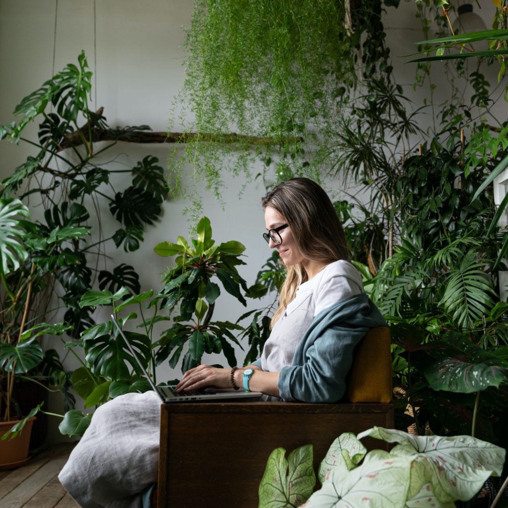 smiling woman gardener sitting on chair at cozy home garden, using laptop and talking in video chat